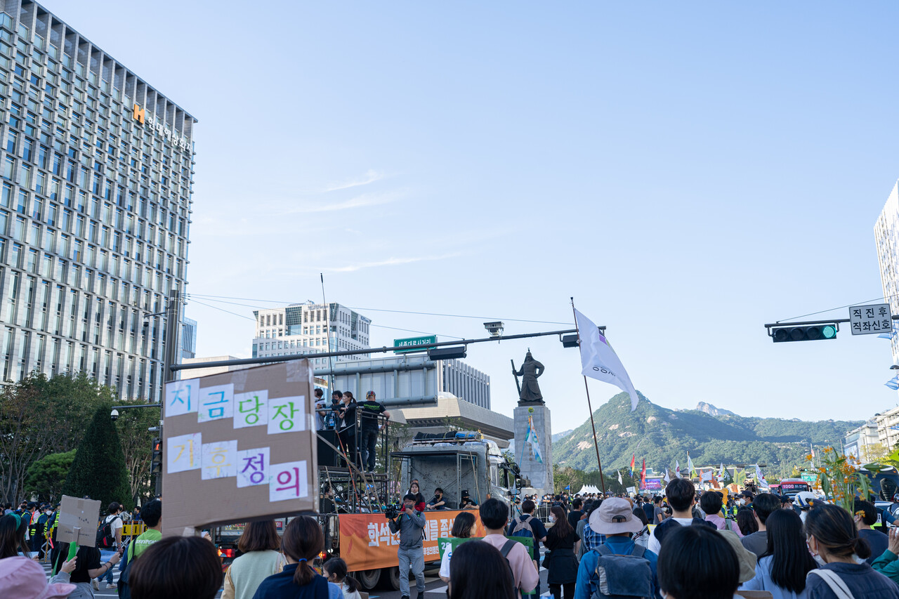 "지금당장 기후정의"라고 적힌 피켓을 든 시민과 행진 중인 시민들의 모습 (사진 : 김연웅 기자)
